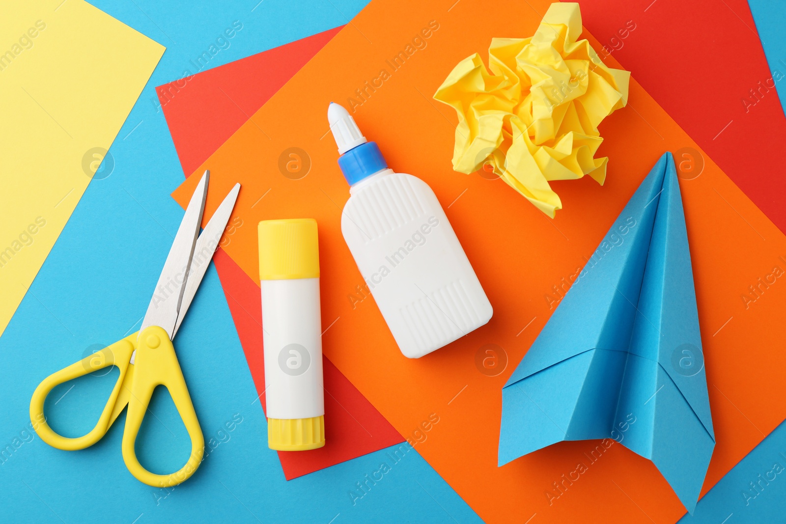 Photo of Glue, colorful paper and scissors on light blue background, flat lay