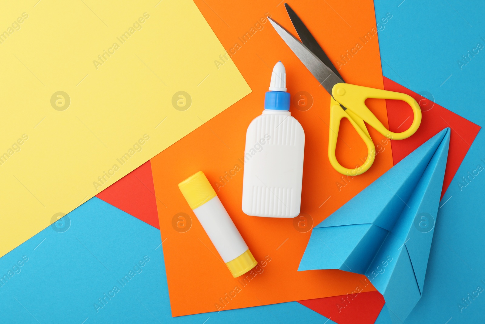 Photo of Glue, colorful paper and scissors on light blue background, flat lay