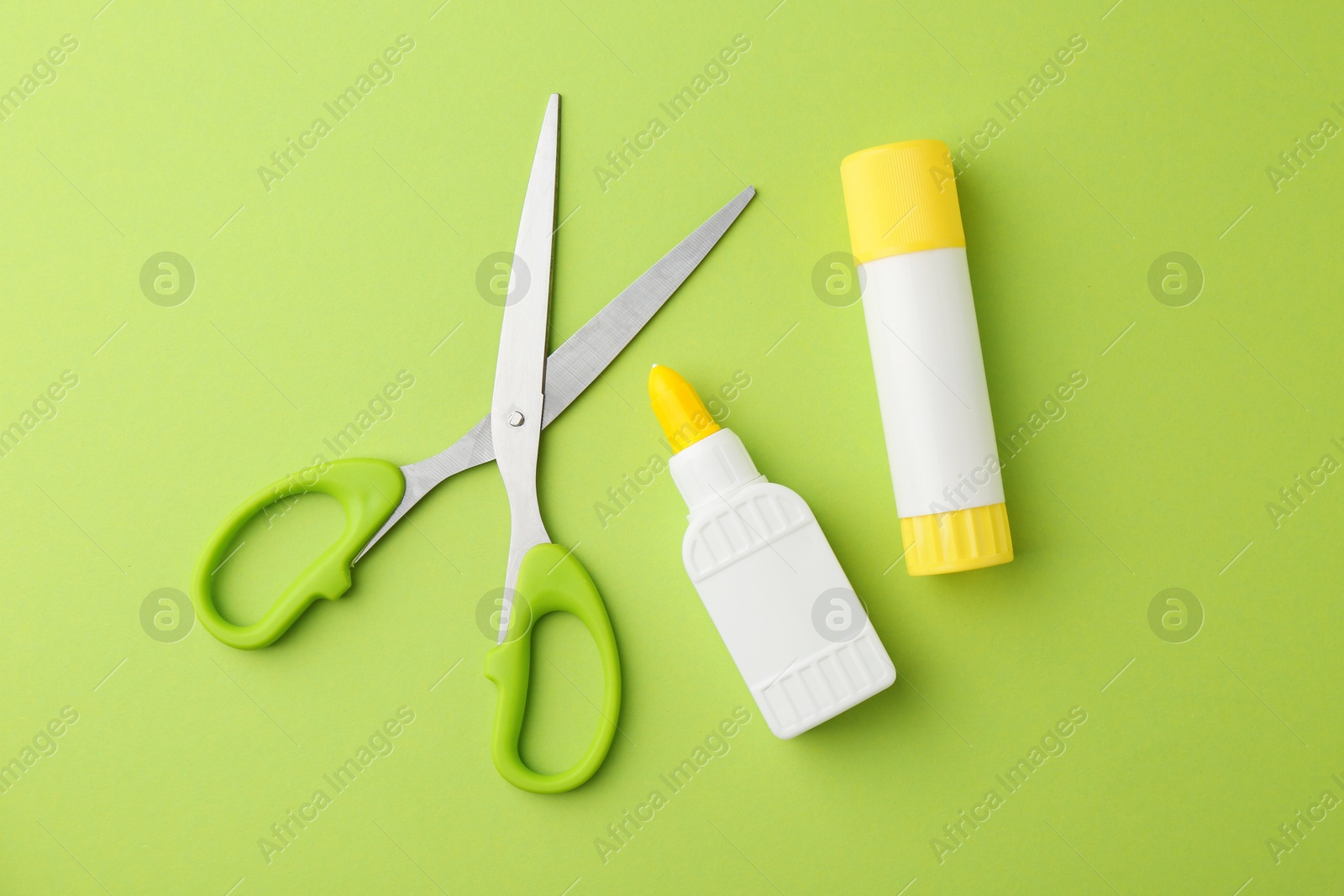 Photo of Different types of glue and scissors on green background, flat lay