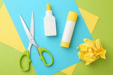 Photo of Different types of glue, colorful paper and scissors on green background, flat lay