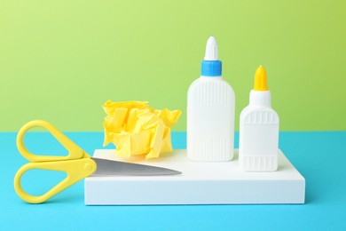 Photo of Bottles of glue, crumpled paper and scissors on color background, closeup