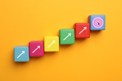 Image of Colorful cubes with arrows and last one with target on yellow background, top view. Steps to success concept