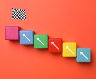 Image of Colorful cubes with arrows and last one with finish flag on dark orange background, top view. Steps to success concept