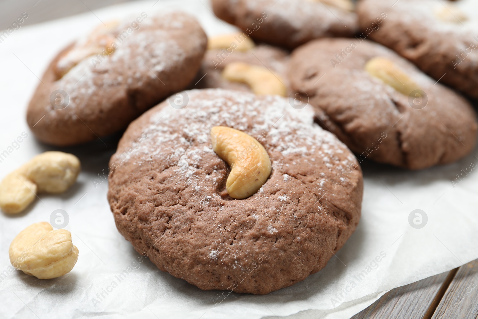 Photo of Delicious chocolate cookies with cashew nuts and powdered sugar on table, closeup