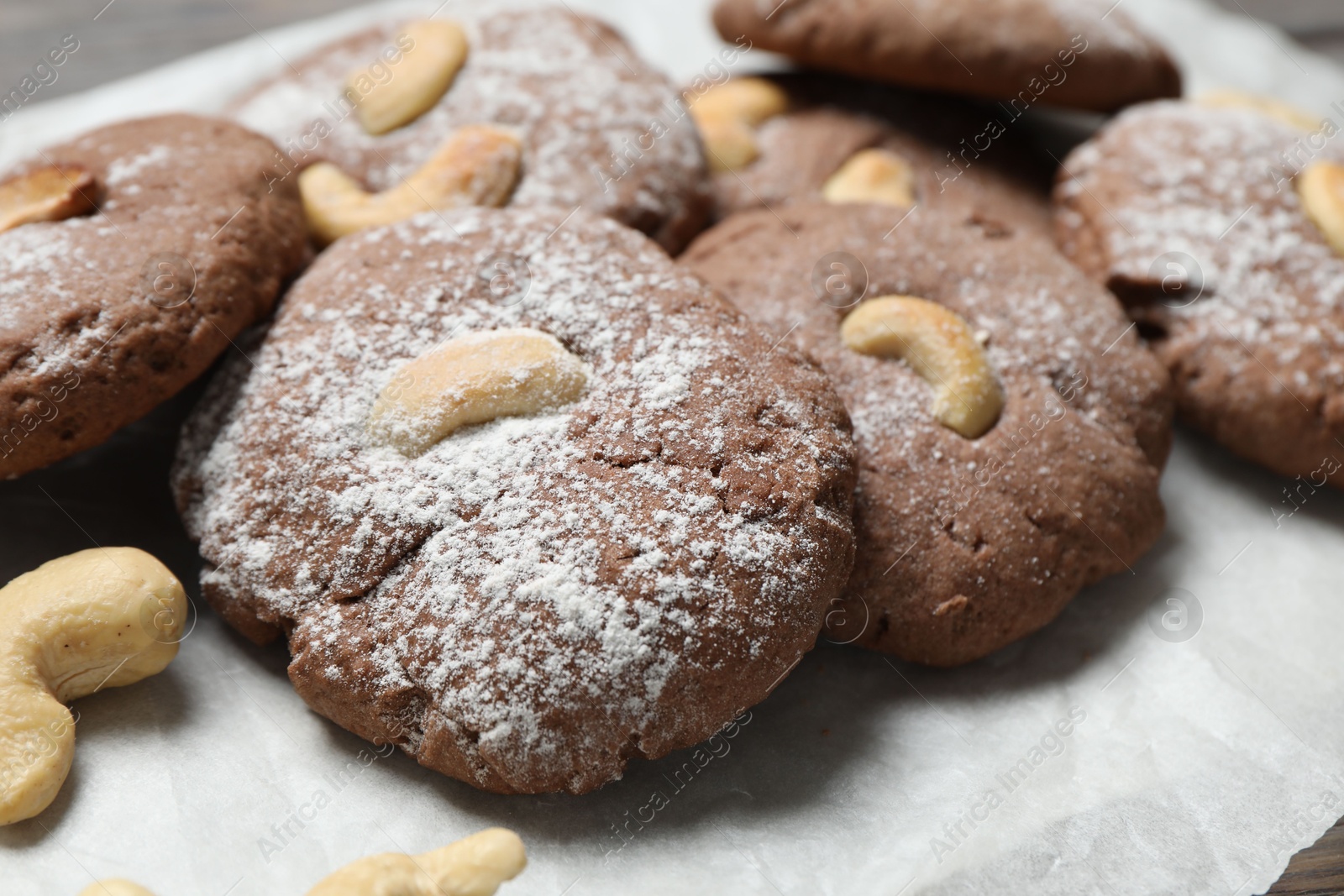 Photo of Delicious chocolate cookies with cashew nuts and powdered sugar on table, closeup