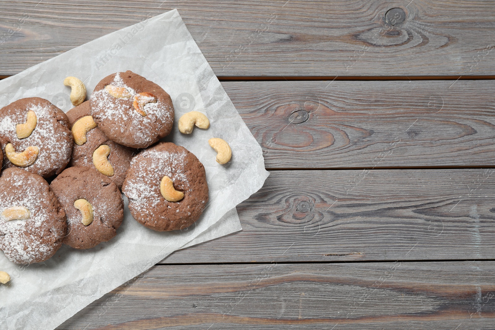 Photo of Delicious chocolate cookies with cashew nuts and powdered sugar on wooden table, top view. Space for text