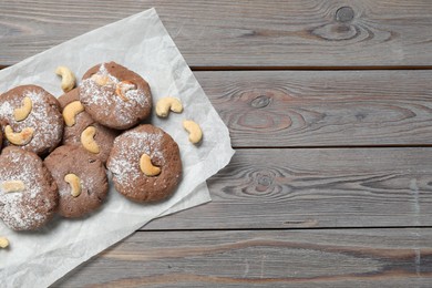 Photo of Delicious chocolate cookies with cashew nuts and powdered sugar on wooden table, top view. Space for text