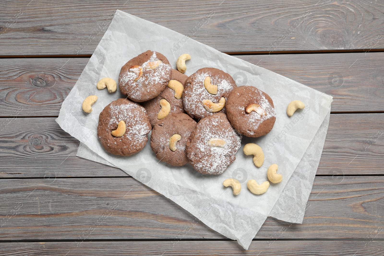 Photo of Delicious chocolate cookies with cashew nuts and powdered sugar on wooden table, top view