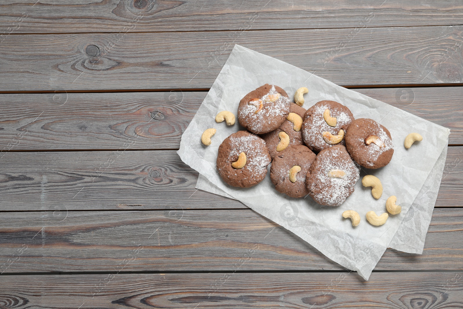 Photo of Delicious chocolate cookies with cashew nuts and powdered sugar on wooden table, top view. Space for text