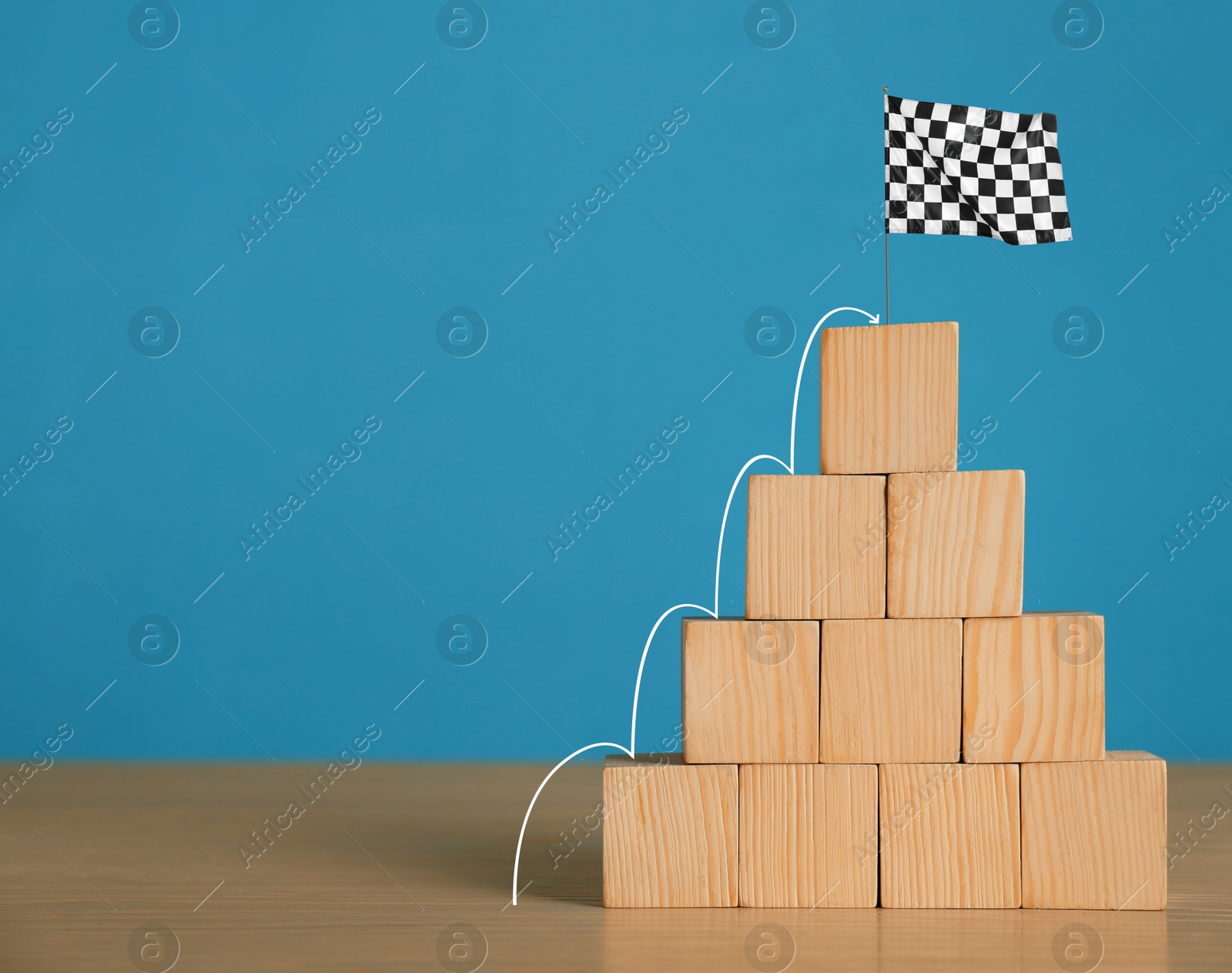 Image of Pyramid made of wooden cubes with finish flag on top against light blue background. Arrow showing way to goal. Steps to success concept