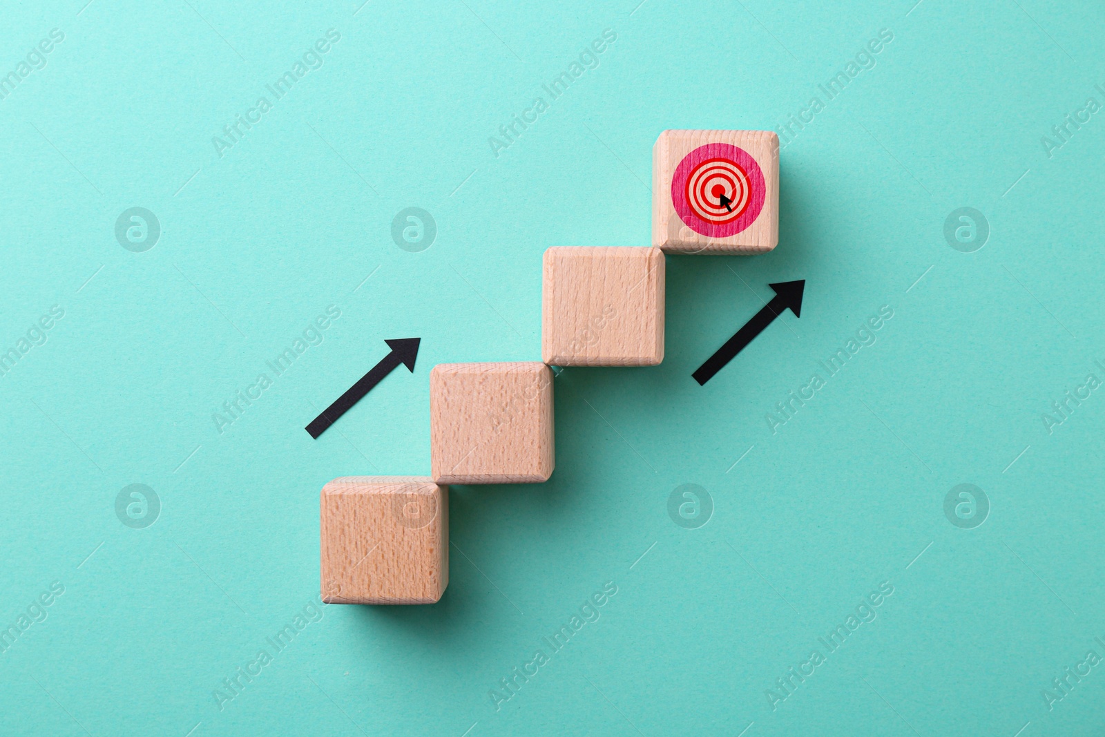 Image of Wooden cubes and last one witn target on turquoise background, top view. Arrows showing direction to goal. Steps to success concept