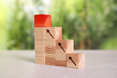 Image of Stair made of wooden blocks on table. Cubes with arrows showing way to red one. Steps to success concept