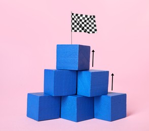 Image of Pyramid made of blue cubes with finish flag on top against pink background. Arrows showing way to goal. Steps to success concept