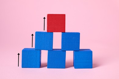 Image of Pyramid made of wooden blocks on pink background. Cubes and arrows showing way to red one. Steps to success concept