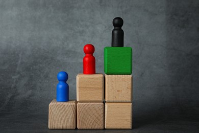 Image of Stair made of wooden cubes as way to goal. Figures on different blocks as stages, black one on top. Steps to success concept