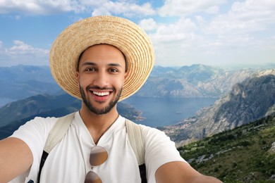 Image of Smiling young man in straw hat taking selfie in mountains