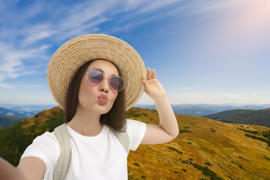 Beautiful woman in straw hat taking selfie in mountains