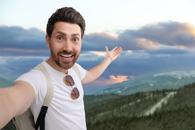 Happy man with backpack taking selfie in mountains