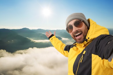 Image of Happy man in hat and sunglasses taking selfie in mountains