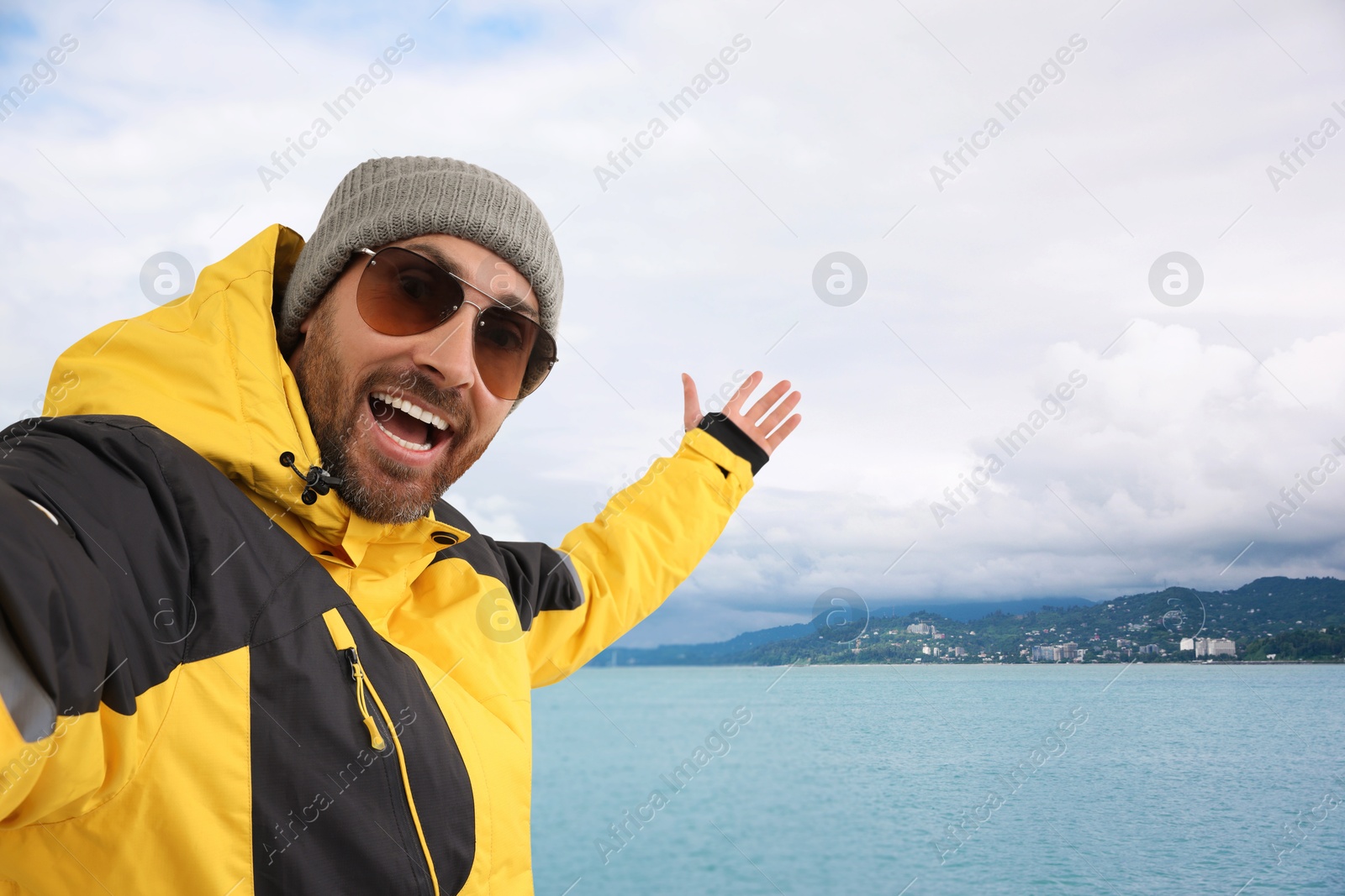 Image of Happy man in hat and sunglasses taking selfie near sea