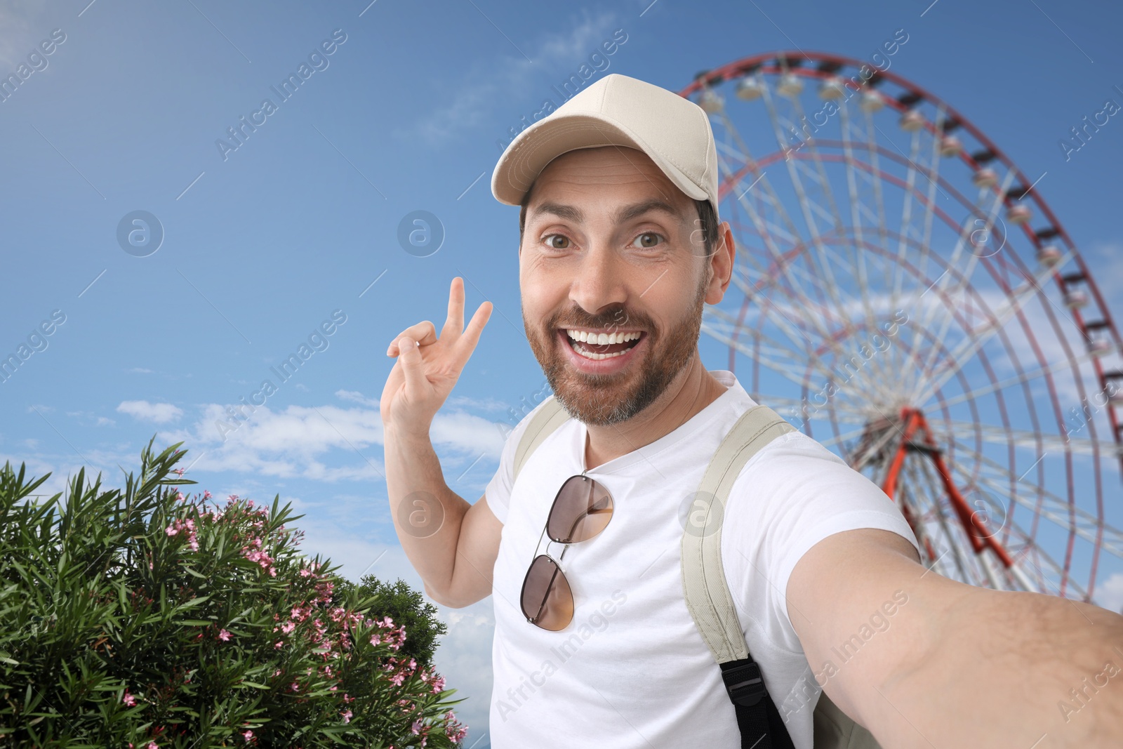 Image of Happy man in cap taking selfie near Ferris wheel