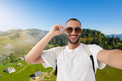 Image of Happy man with sunglasses taking selfie in mountains