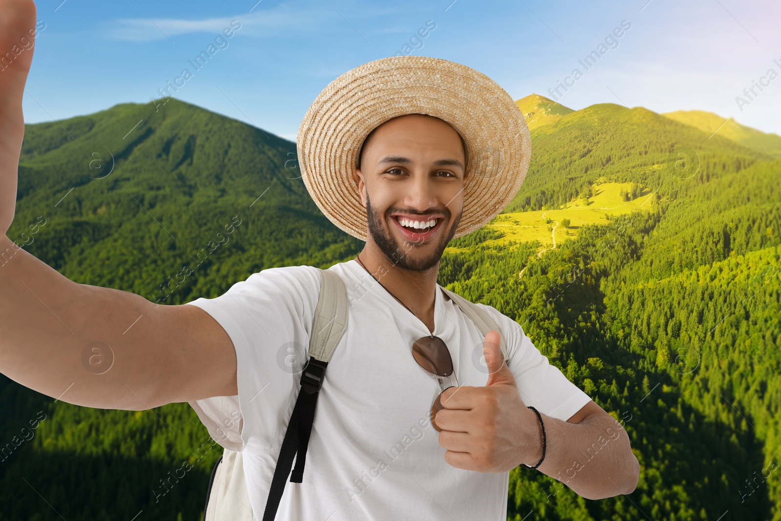 Image of Smiling young man in straw hat taking selfie in mountains