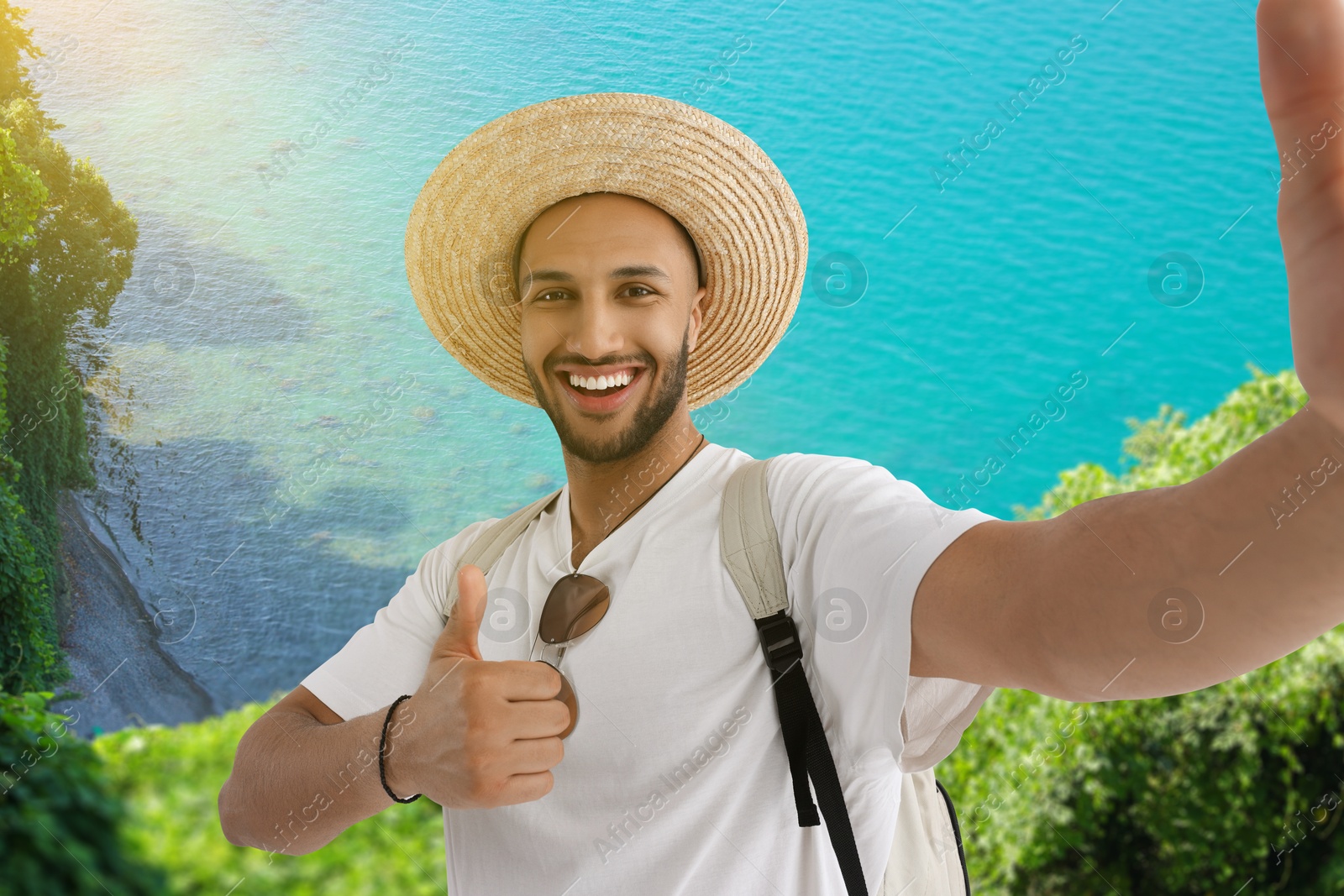 Image of Smiling young man in straw hat taking selfie near sea