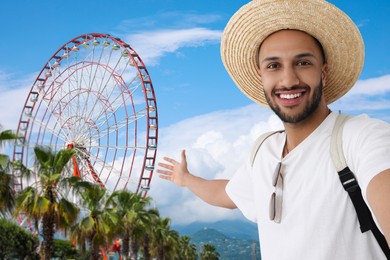 Smiling young man in straw hat taking selfie near Ferris wheel