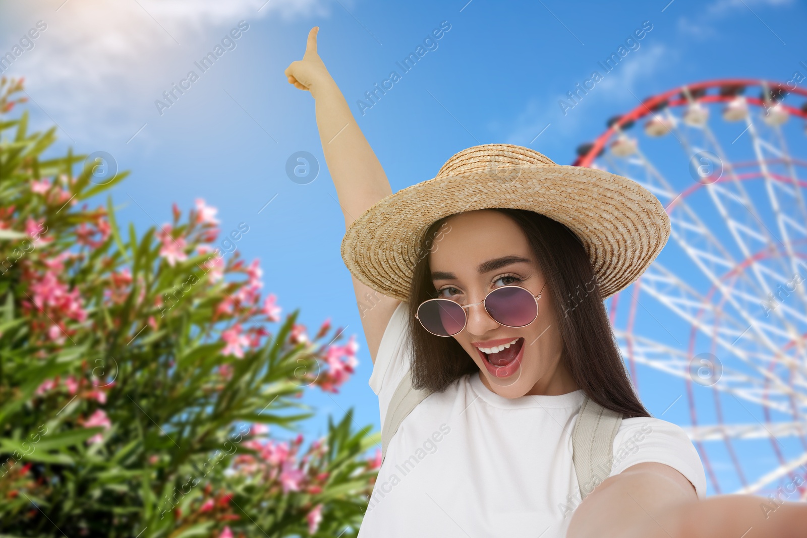 Image of Happy woman in straw hat taking selfie near Ferris wheel