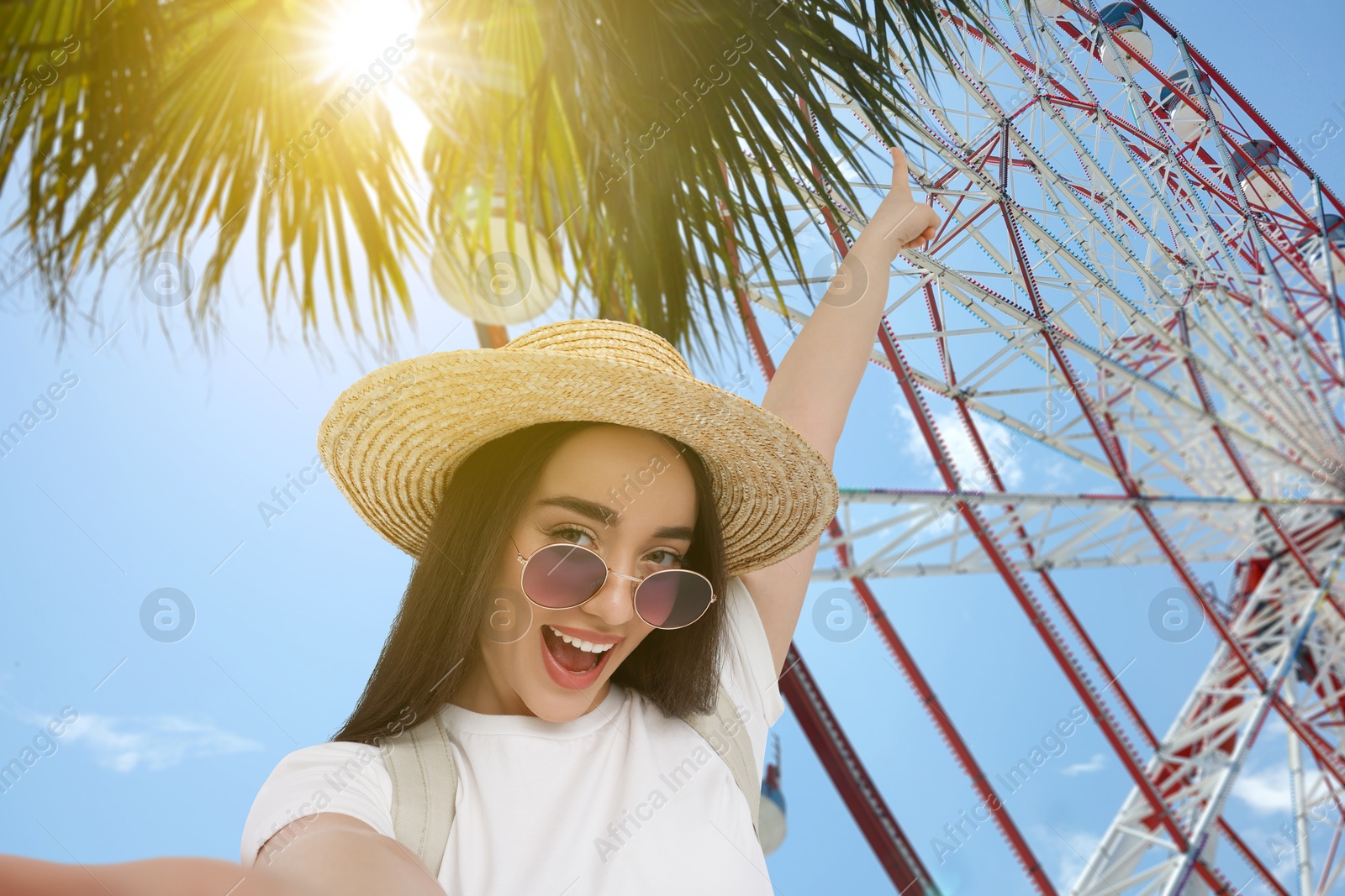 Image of Happy woman in straw hat taking selfie near Ferris wheel