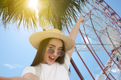 Happy woman in straw hat taking selfie near Ferris wheel