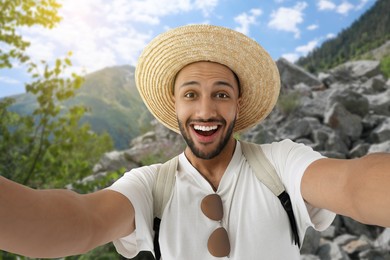 Image of Smiling young man in straw hat taking selfie in mountains