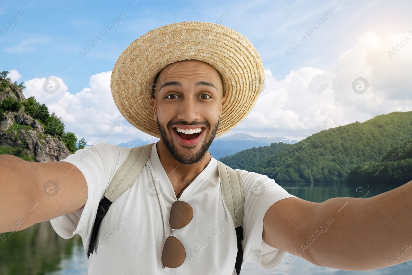 Image of Smiling young man in straw hat taking selfie near lake