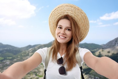 Image of Happy woman in straw hat taking selfie in mountains