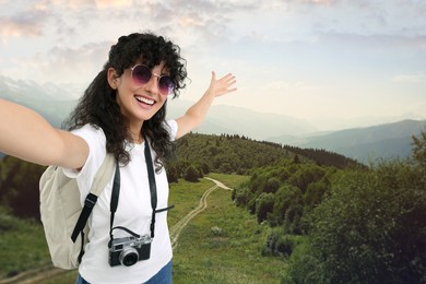 Beautiful woman with sunglasses and camera taking selfie in mountains