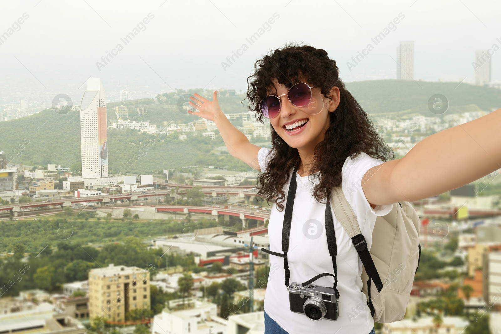 Image of Beautiful woman with sunglasses and camera taking selfie against city