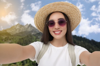 Happy woman in straw hat taking selfie in mountains