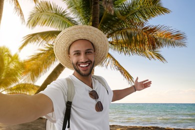 Smiling young man in straw hat taking selfie at beach