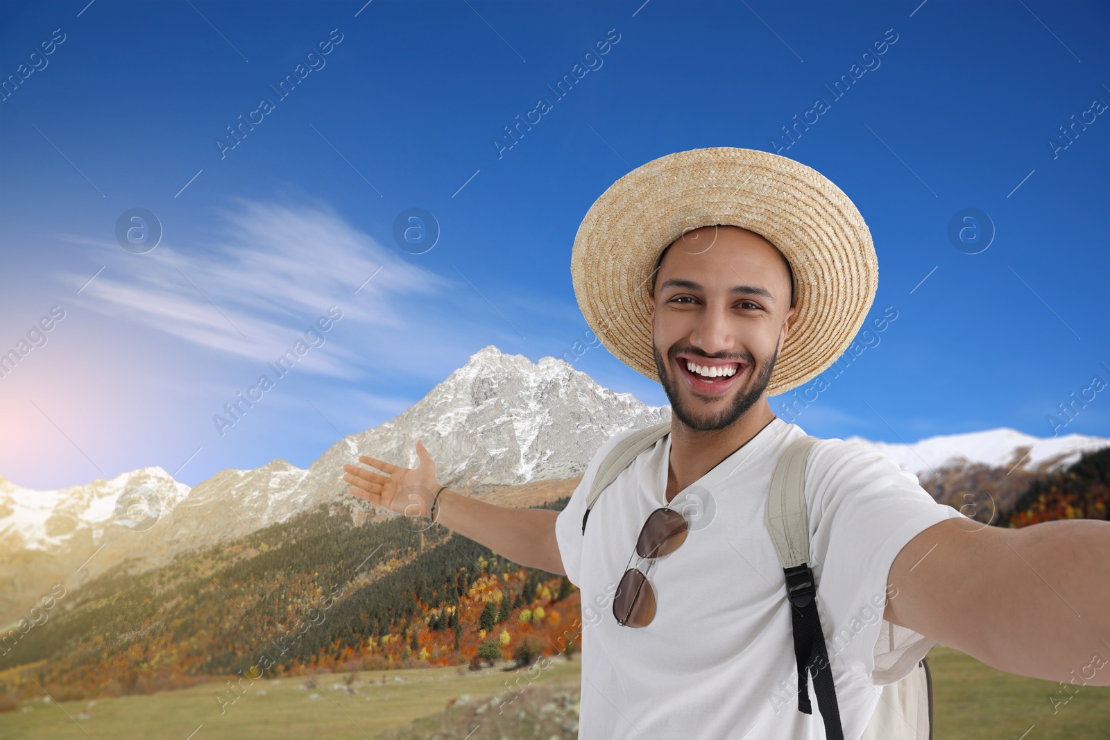 Image of Smiling young man in straw hat taking selfie in mountains