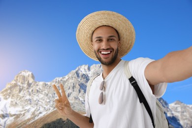 Smiling young man in straw hat taking selfie in mountains