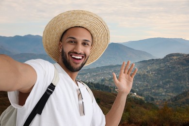 Image of Smiling young man in straw hat taking selfie in mountains