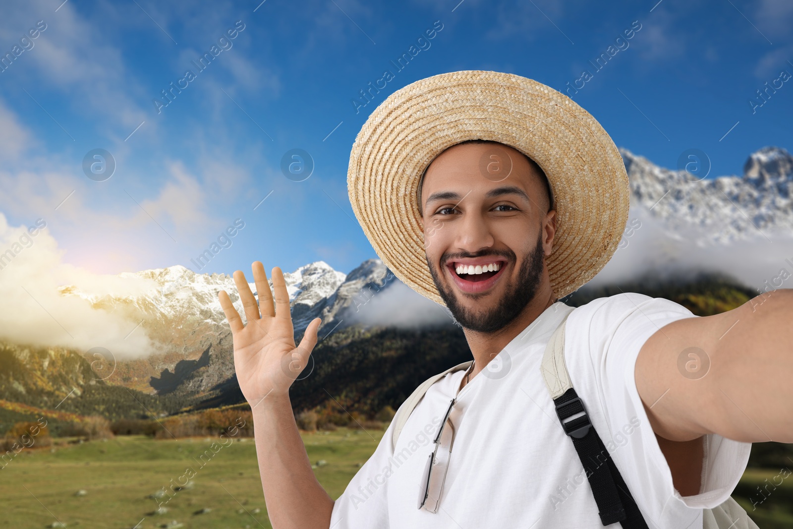 Image of Smiling young man in straw hat taking selfie in mountains