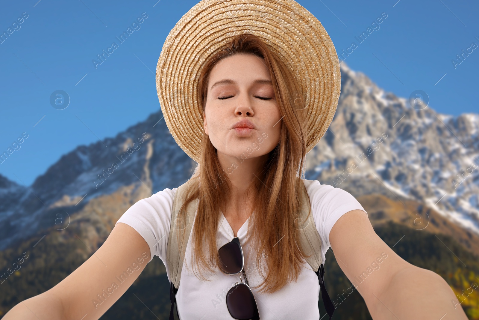 Image of Happy woman in straw hat taking selfie in mountains