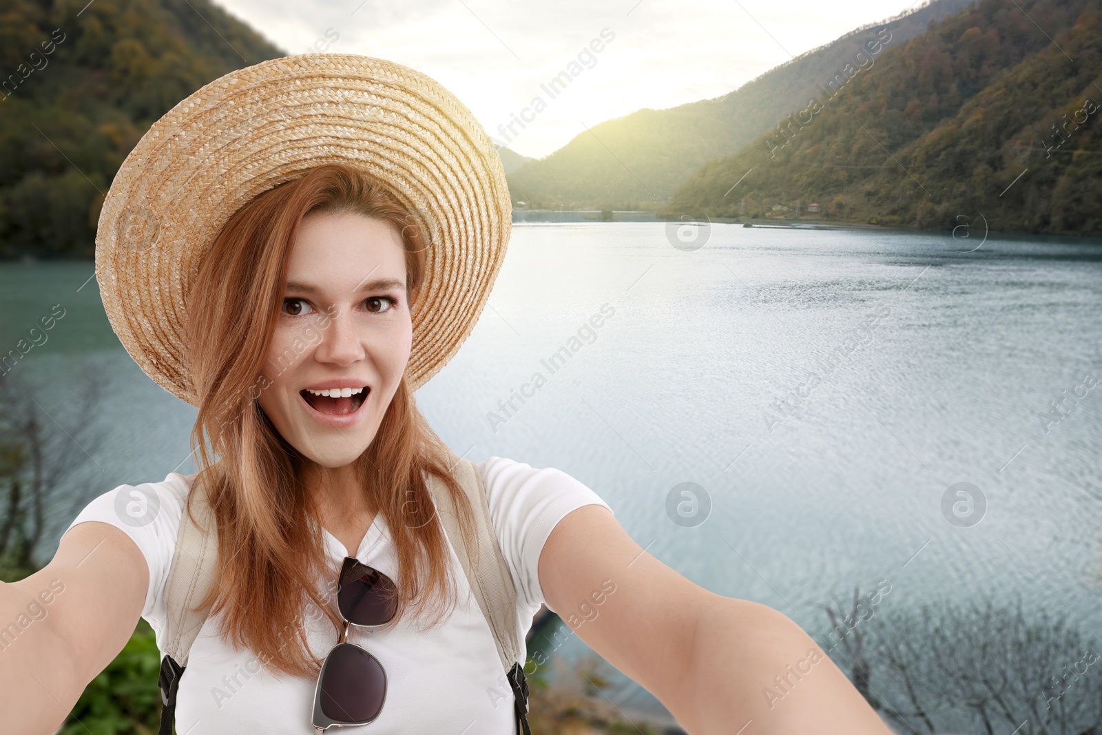 Image of Happy woman in straw hat taking selfie near lake