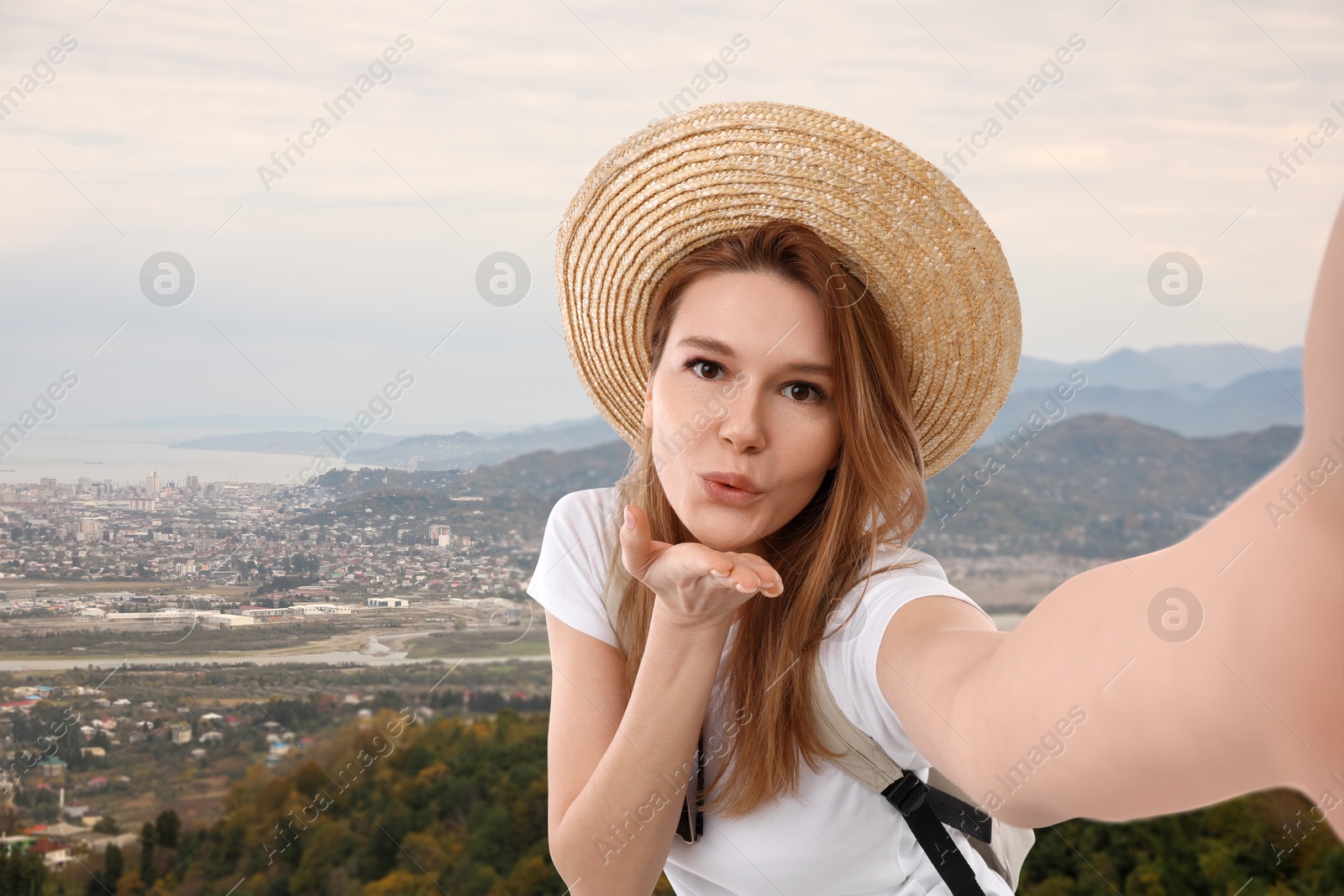 Image of Happy woman in straw hat taking selfie in mountains