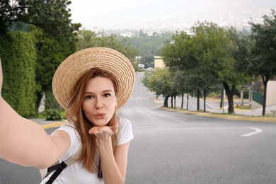 Image of Happy woman in straw hat taking selfie in city