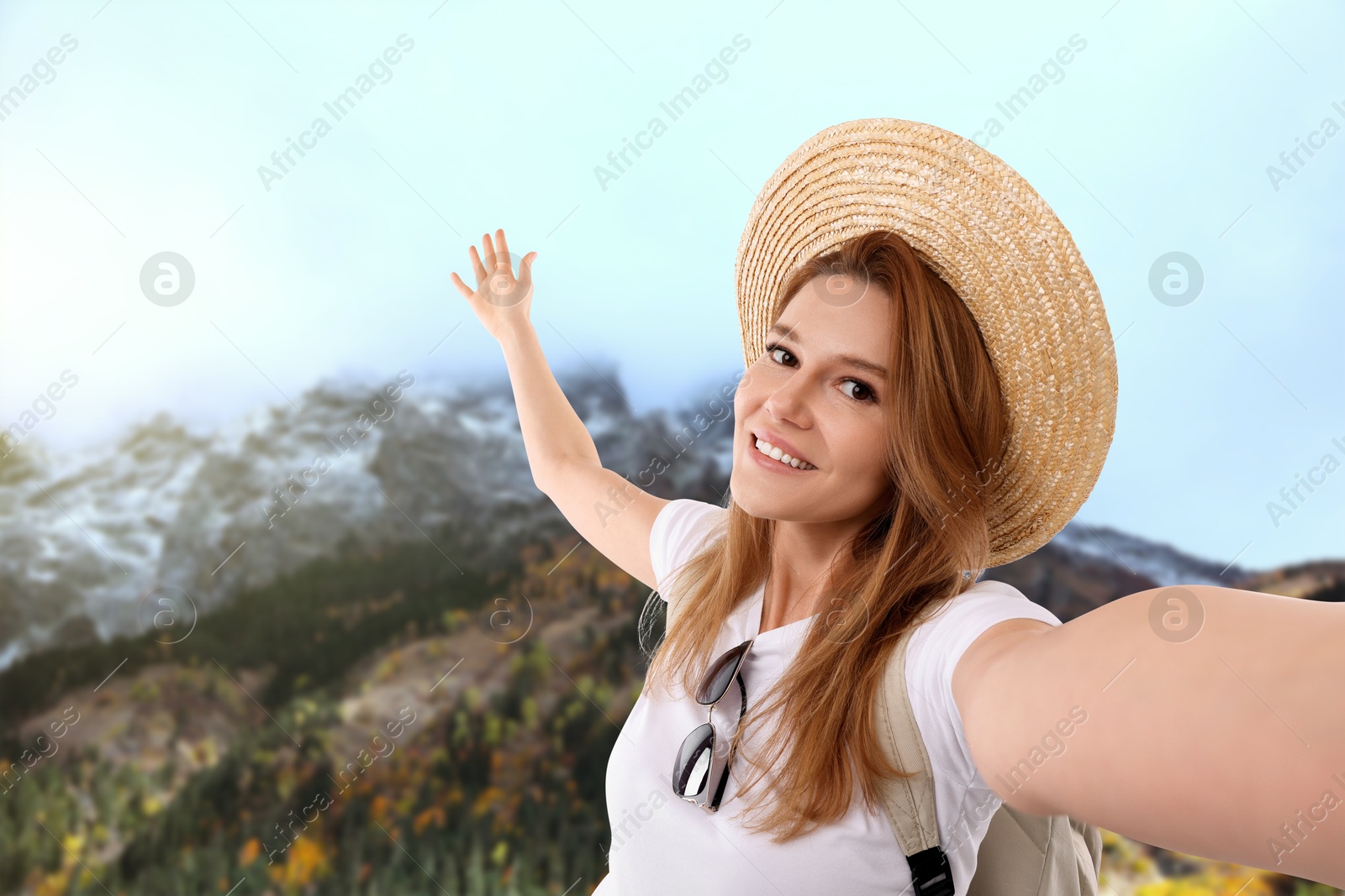 Image of Happy woman in straw hat taking selfie in mountains