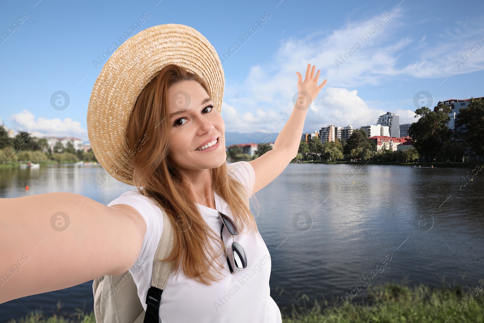 Image of Happy woman in straw hat taking selfie near river