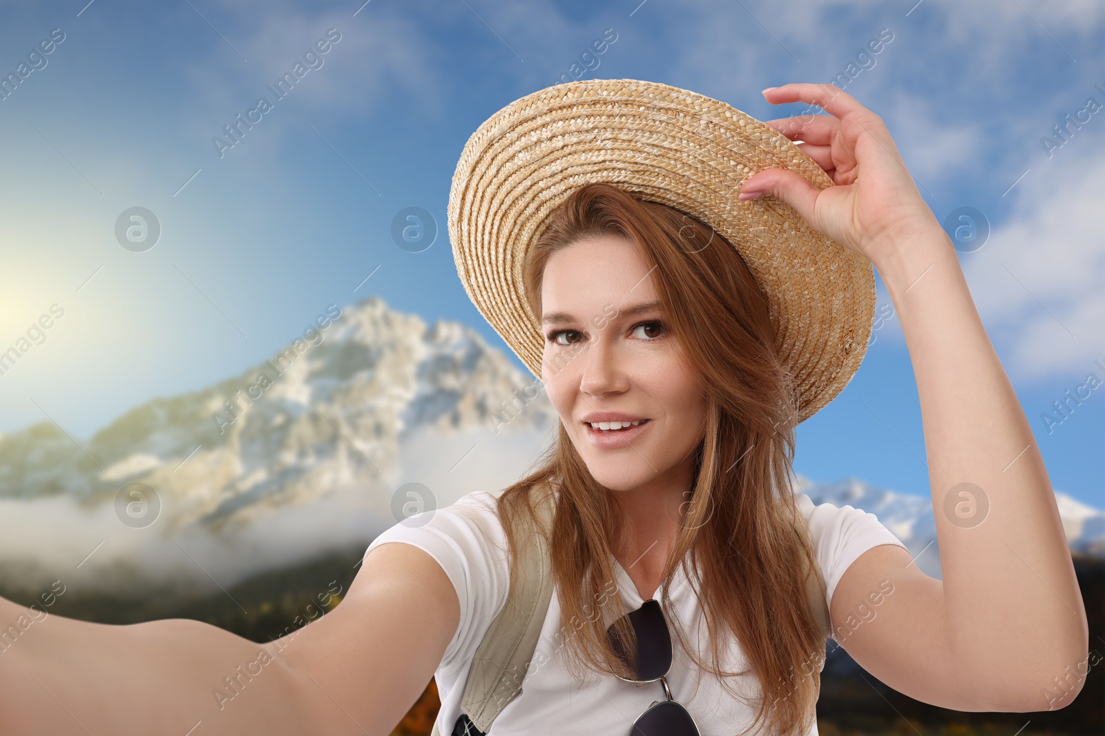 Image of Happy woman in straw hat taking selfie in mountains